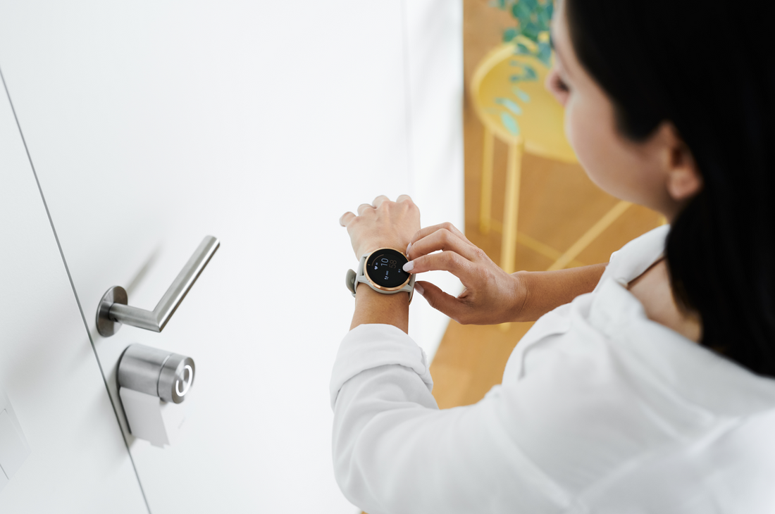 Person bedient eine Smartwatch vor einer weißen Wohnungstür mit Nuki Smart Lock am Zylinder