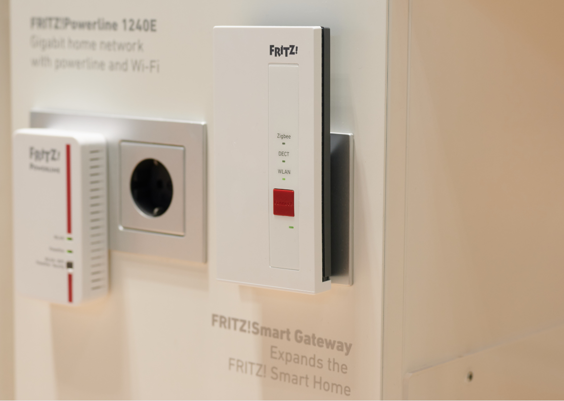 FRITZ!Smart Gateway in einer Wandsteckdose, daneben ein FRITZ!Powerline 1240E, LEDs für Zigbee, DECT und WLAN