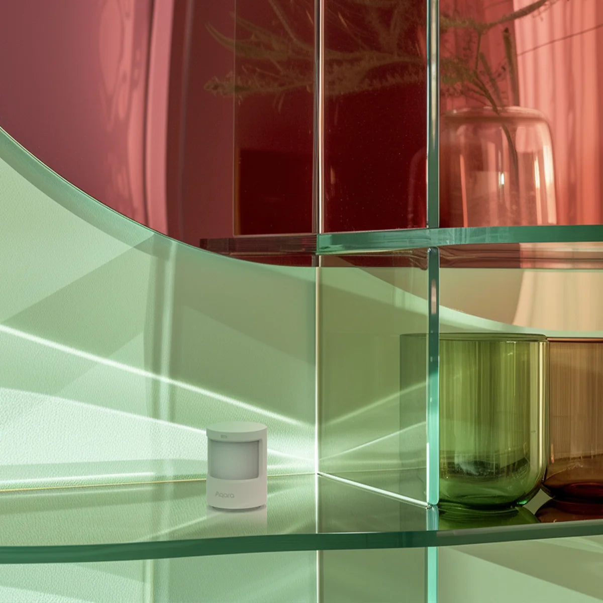 Der Aqara P2 steht unauffällig auf einem Glasregal zwischen grünen und roten Glasvasen