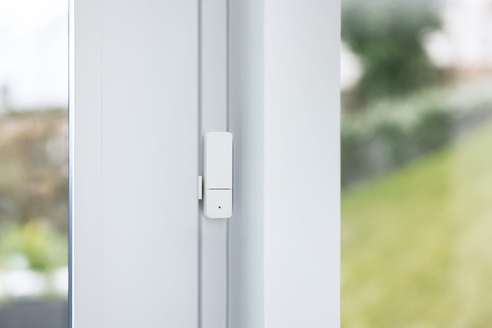 Tür-/Fensterkontakt II [+M] am weißen Fensterrahmen montiert, Magnet auf dem Flügel, Garten dahinter
