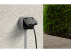 Eve Energy Outdoor mit Wassertropfen an einer Hauswand, angeschlossenes Kabel führt nach unten