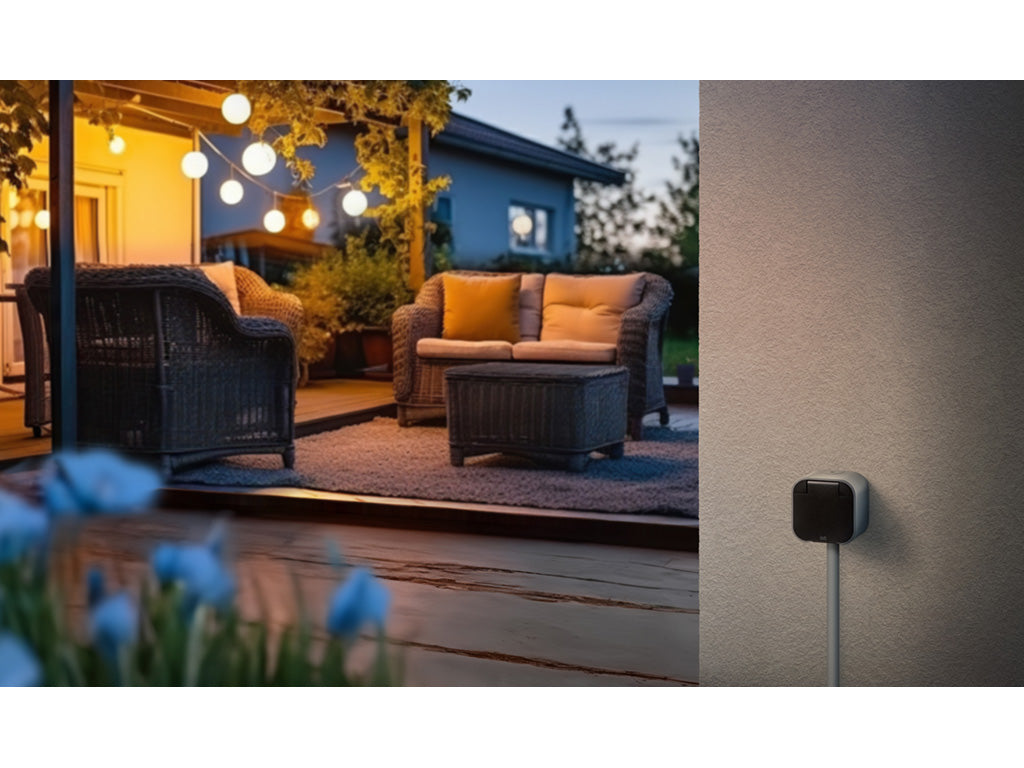 Eve Energy Outdoor an der Hauswand, daneben beleuchtete Terrasse mit Lichterkette in der Dämmerung