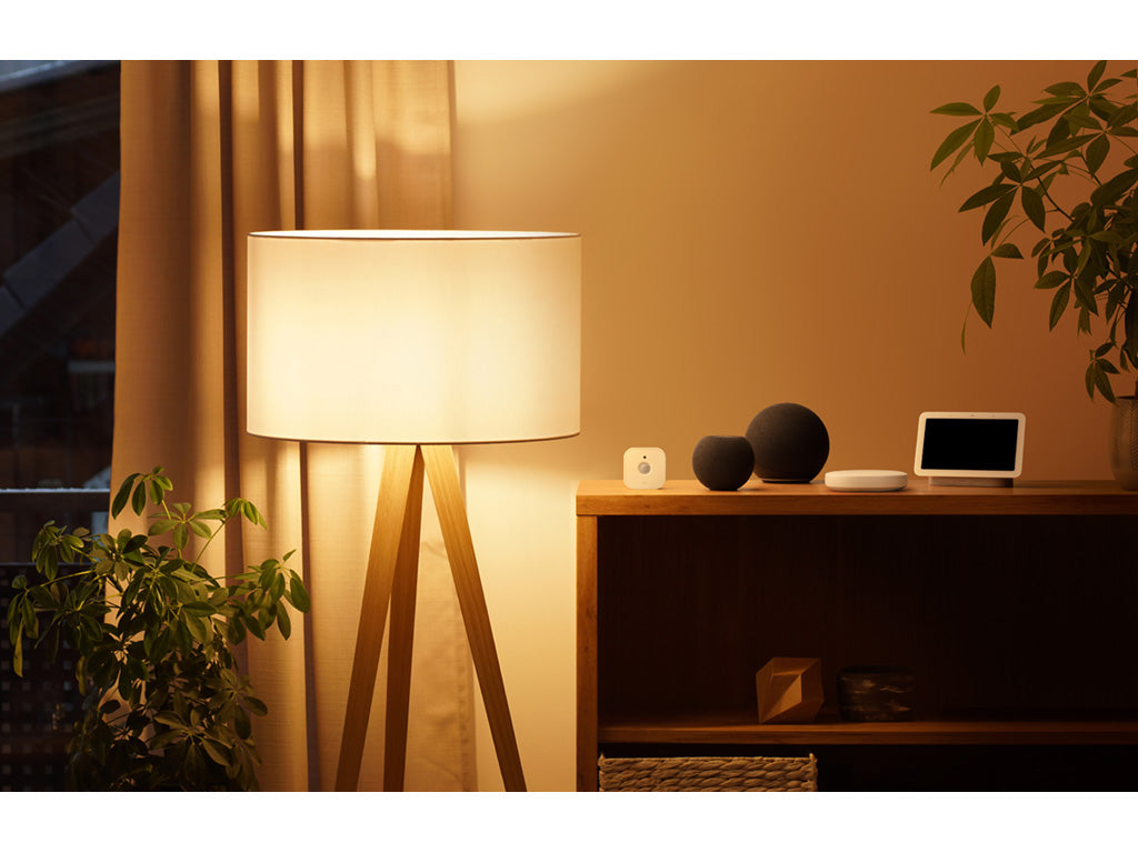 Eve Motion auf einem Sideboard neben zwei Lautsprechern und Smart Display, Stehlampe leuchtet daneben