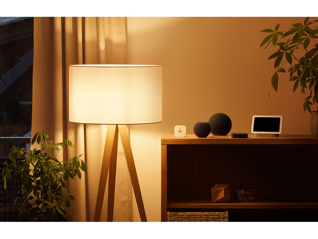 Eve Motion im abendlichen Wohnzimmer, daneben dunkle Lautsprecher und Smart Display auf der Kommode