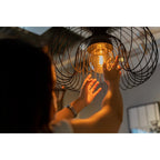 Frau greift an eine Käfig-Pendelleuchte mit warm leuchtender Hama Retro-LED Lampe