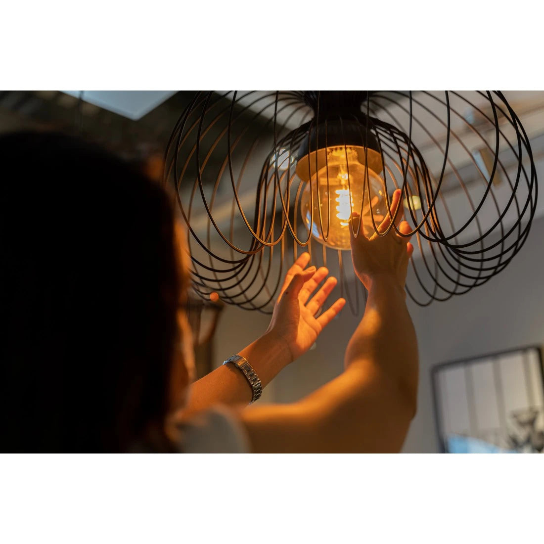 Frau greift an eine Käfig-Pendelleuchte mit warm leuchtender Hama Retro-LED Lampe