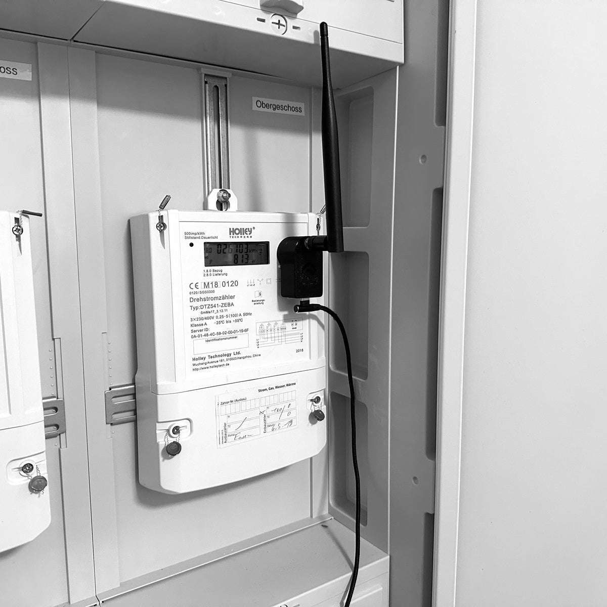 Lesekopf mit LoRa-Funkbrücke auf einem Drehstromzähler im Zählerschrank, Antenne senkrecht nach oben