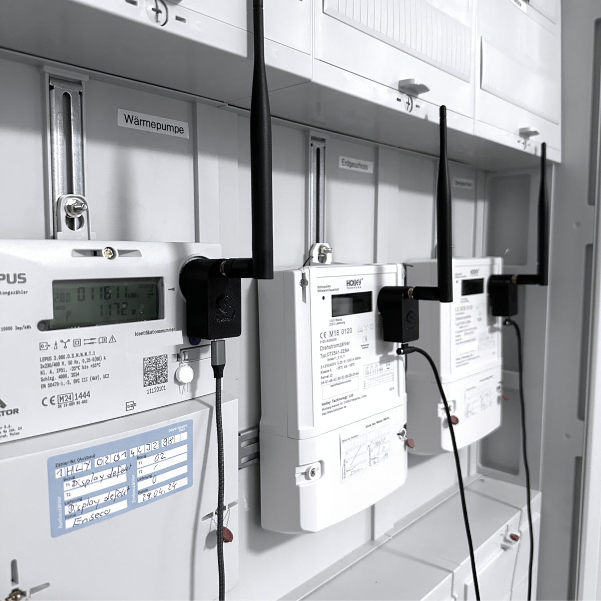 Drei Leseköpfe mit Antennen nebeneinander auf den Zählern für Wärmepumpe und Wohnungen