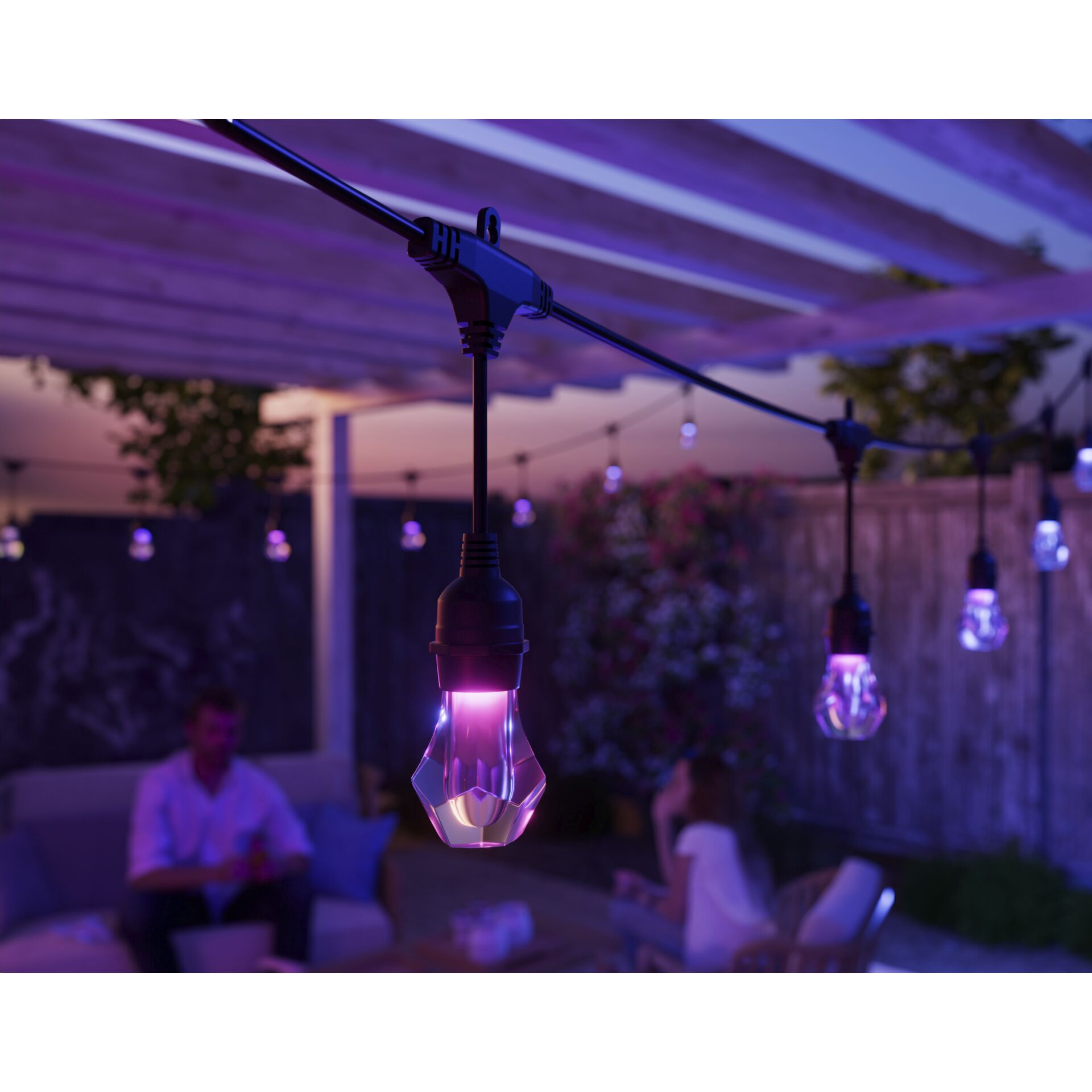 Pink leuchtende Lampe der Nanoleaf Outdoor Light String, dahinter sitzende Gäste auf der Terrasse