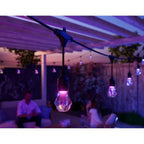 Pink leuchtende Birne des Nanoleaf Outdoor String Light im Vordergrund, zwei Personen sitzen dahinter im Freien
