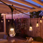 Warmweiß leuchtende Birne des Nanoleaf Outdoor String Light in Nahaufnahme unter einer Holzpergola am Abend