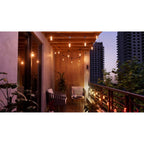 Nanoleaf Outdoor String Light warmweiß auf einem Balkon mit Holzdecke und Sesseln, Hochhäuser im Hintergrund
