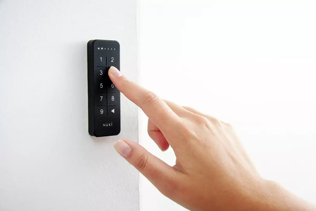 Hand tippt einen Zutrittscode auf dem an einer weißen Außenwand montierten Nuki Keypad ein