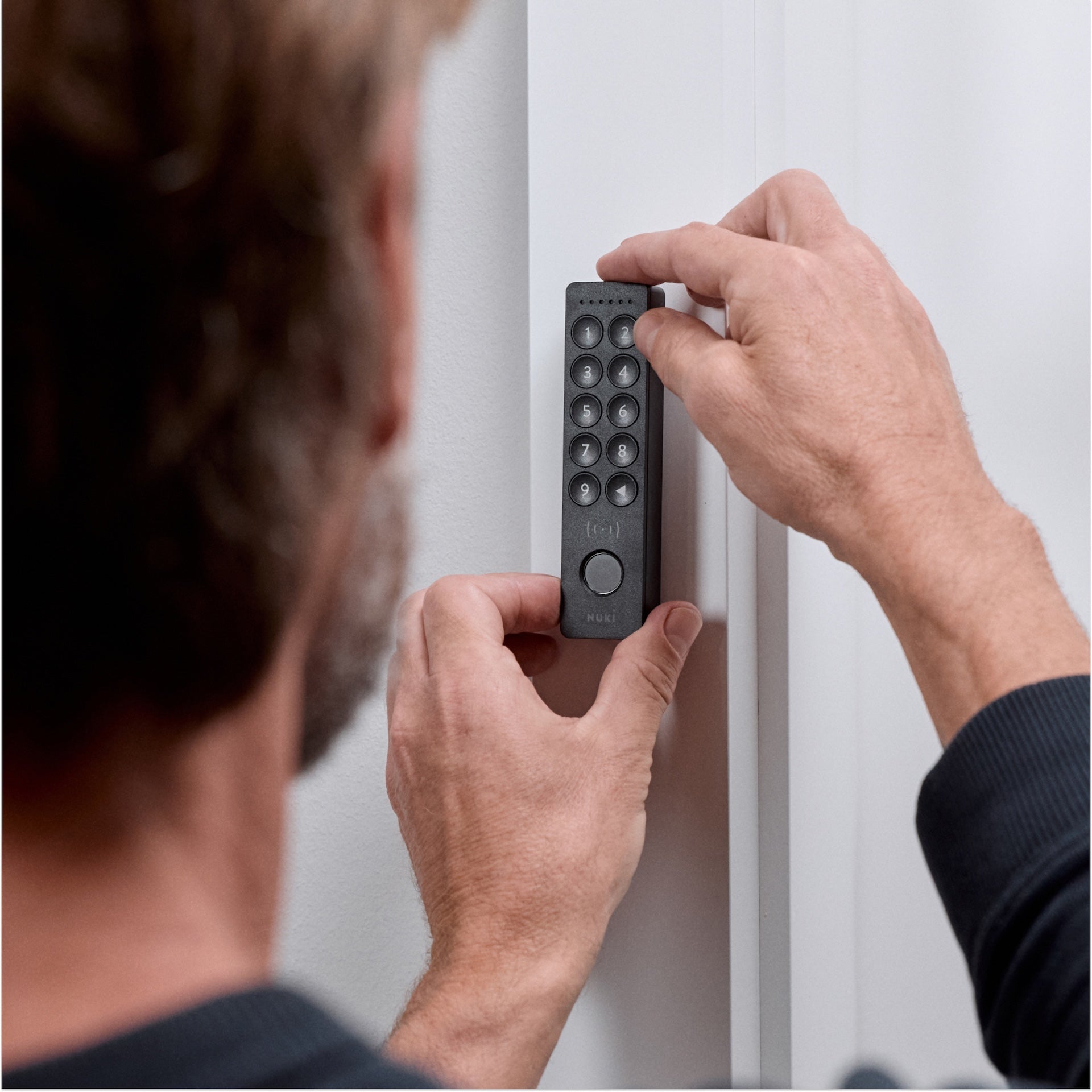 Mann setzt das Nuki Keypad 2 NFC mit beiden Händen an einen weißen Türrahmen