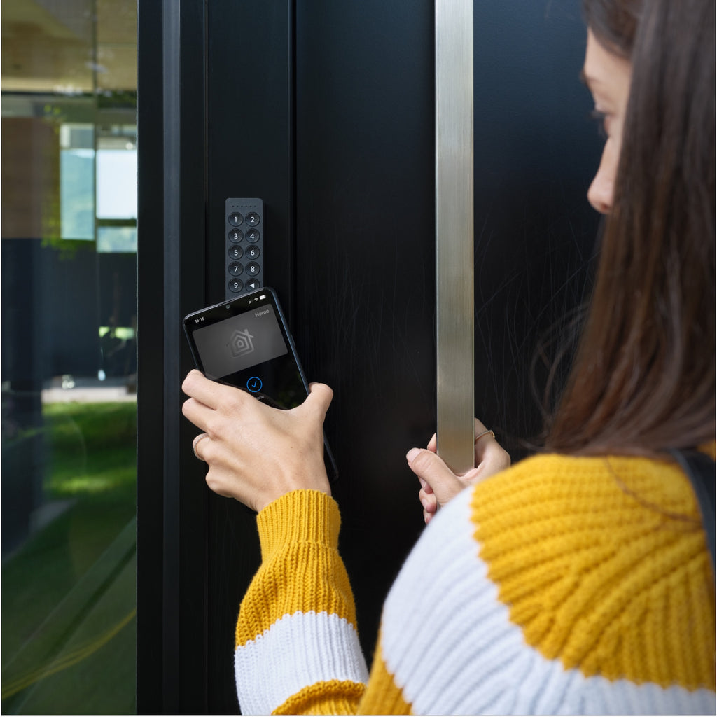 Smartphone wird zum Öffnen vor das am dunklen Türrahmen montierte Nuki Keypad 2 NFC gehalten