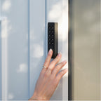 Zeigefinger berührt den Fingerabdrucksensor des Nuki Keypad 2 NFC an einer hellblauen Tür