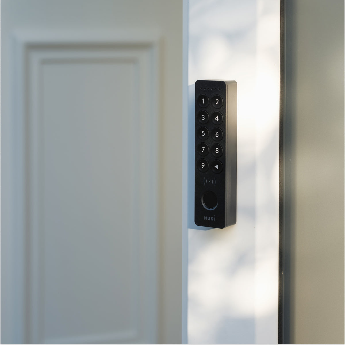 Nuki Keypad 2 NFC seitlich am schmalen Rahmen einer hellen Tür montiert, im Streiflicht fotografiert
