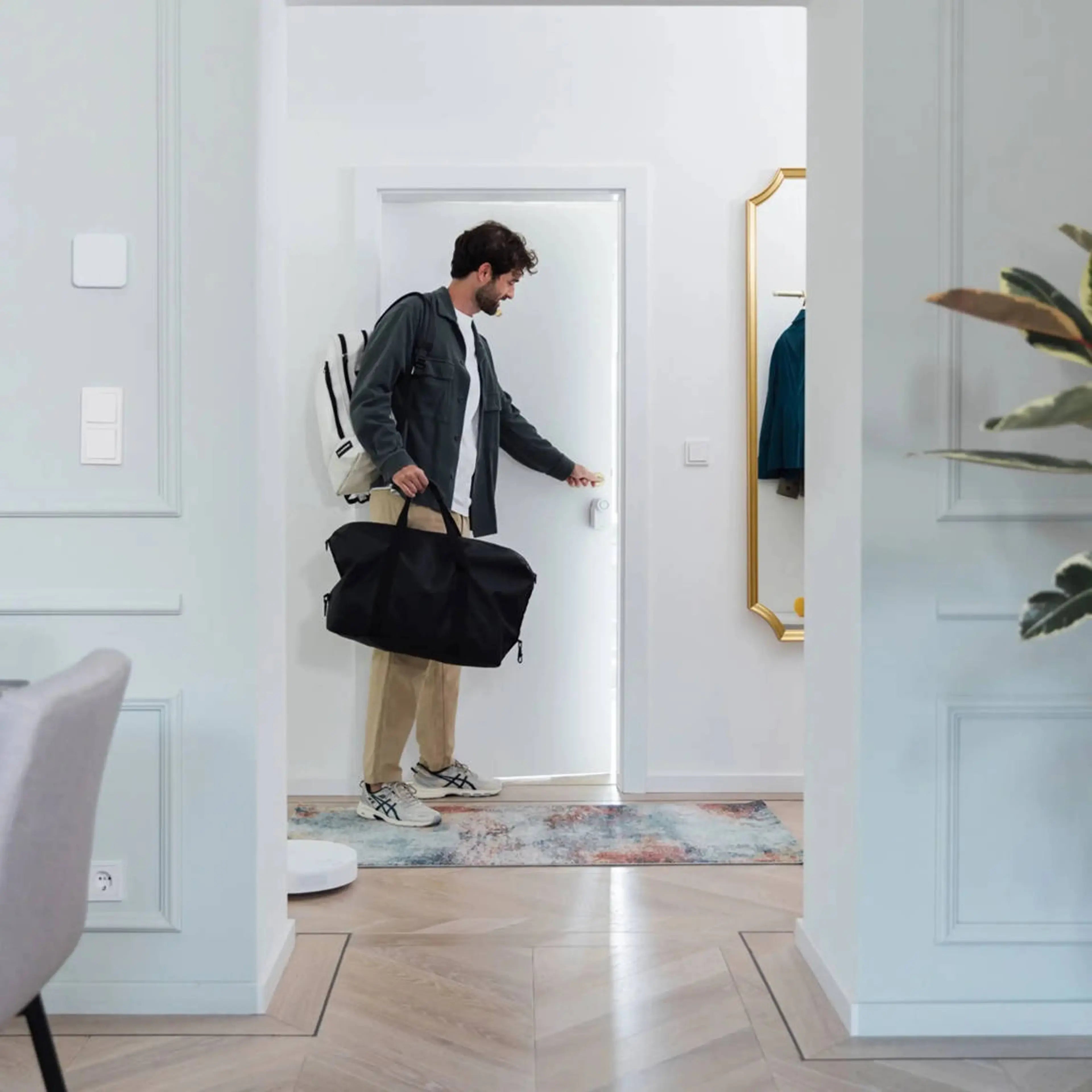 Mann mit Reisetasche tippt im Altbauflur im Vorbeigehen auf das an der Wohnungstür montierte Nuki Smart Lock Go