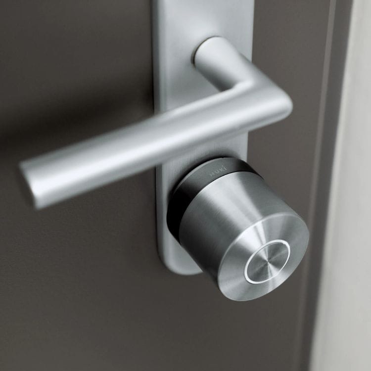Nuki Smart Lock Ultra mit schwarzem Basisring, montiert an einer braungrauen Tür dicht unter dem Türdrücker