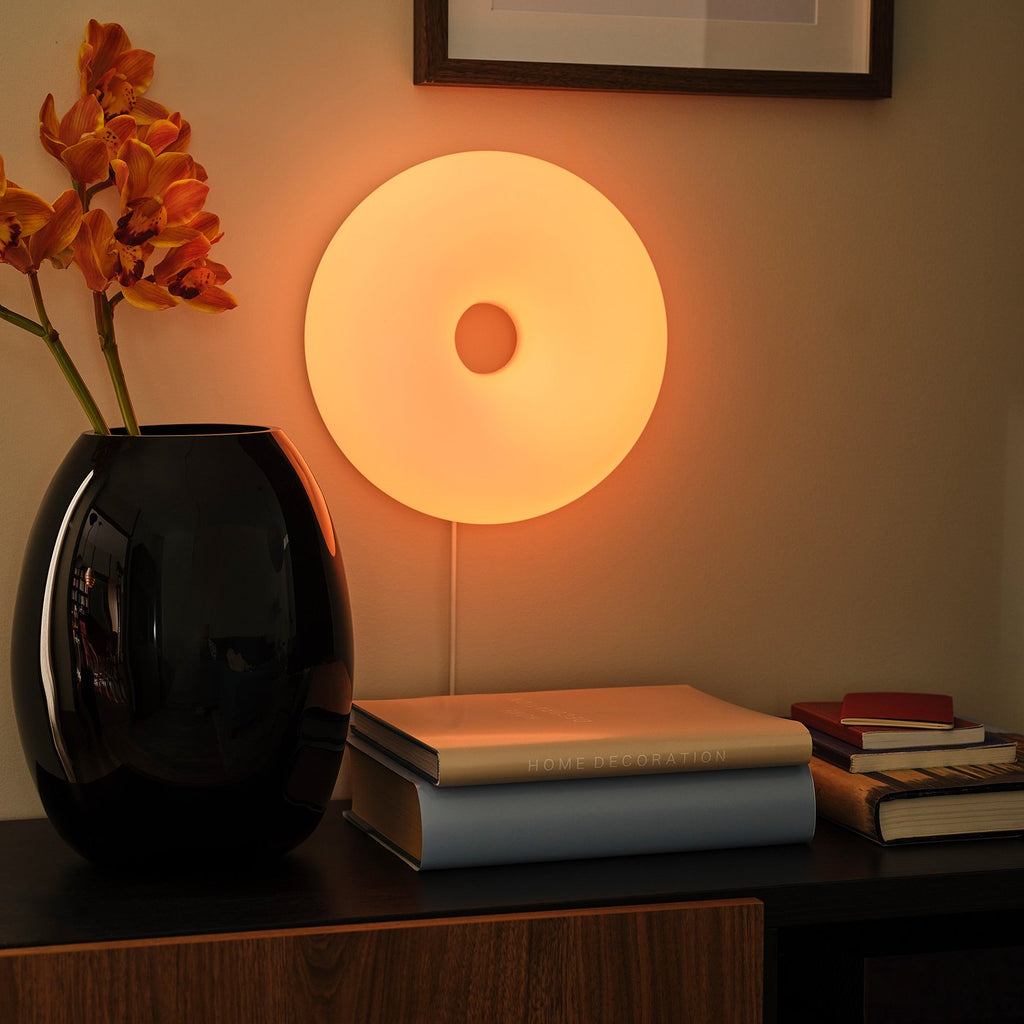 IKEA VARMBLIXT an der Wand montiert, leuchtet orange über einer Kommode mit Büchern und Vase
