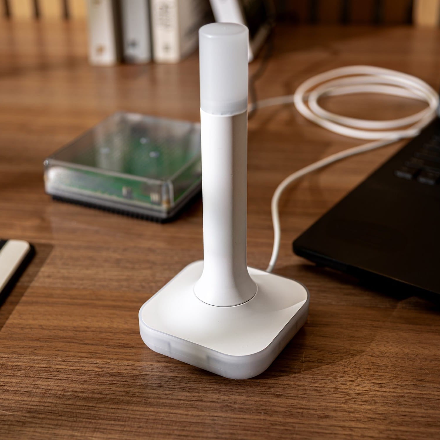 Nahaufnahme des ZBT-2 auf einem Holztisch mit aufgerolltem USB-Kabel, dahinter ein Home Assistant Green