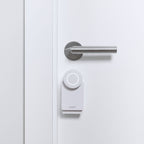 Nuki Smart Lock Go in Weiß, montiert an einer weißen Tür unmittelbar unter dem Edelstahl-Türdrücker