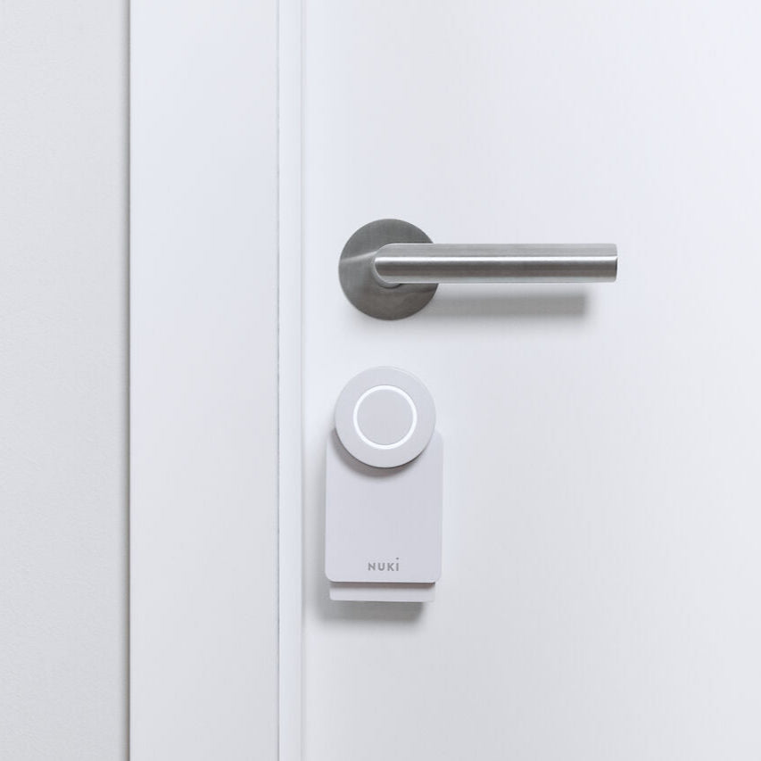 Nuki Smart Lock Go in Weiß, montiert an einer weißen Tür unmittelbar unter dem Edelstahl-Türdrücker