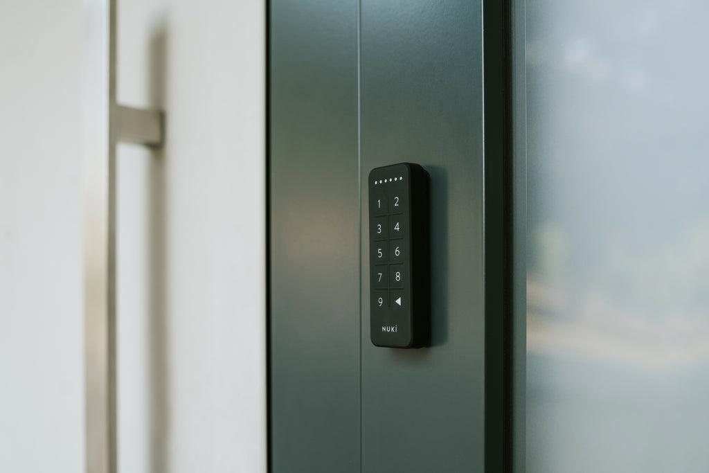 Nuki Keypad seitlich auf den dunkelgrünen Türrahmen einer Glastür geklebt, Tasten in Nahaufnahme