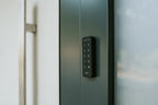 Nuki Keypad seitlich auf den dunkelgrünen Türrahmen einer Glastür geklebt, Tasten in Nahaufnahme