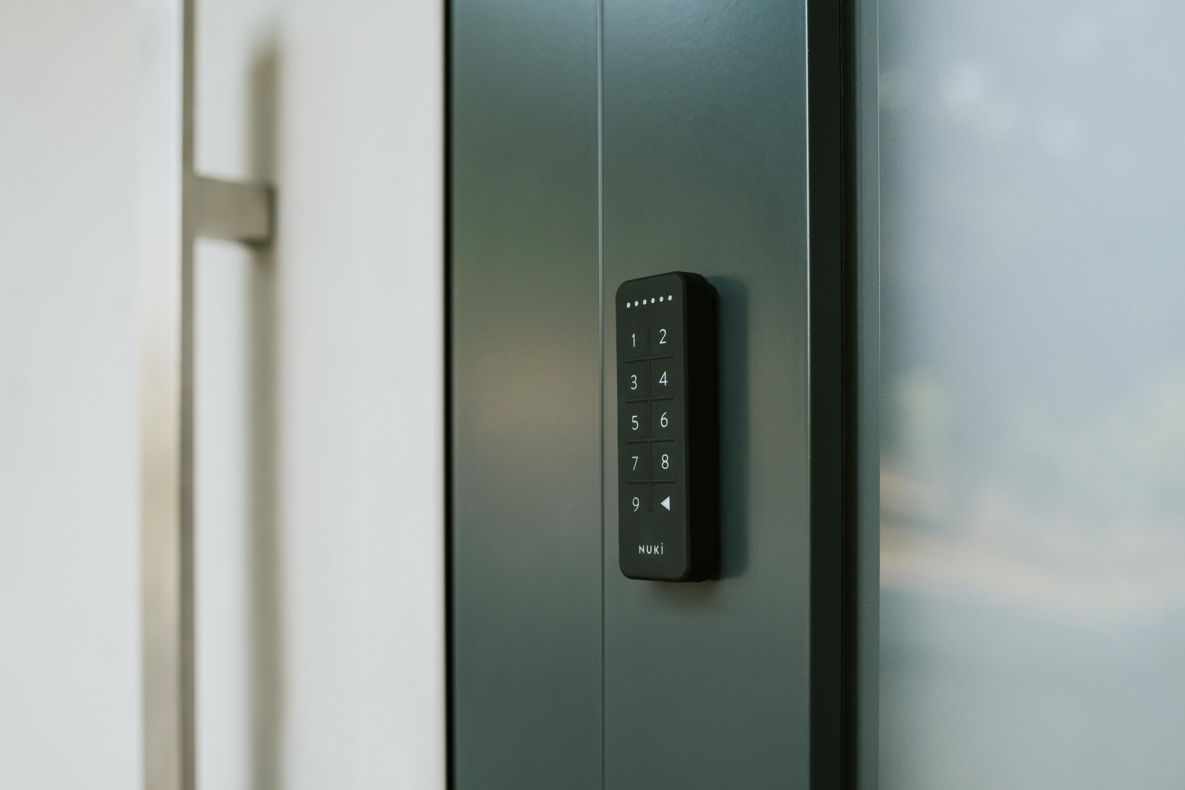 Nuki Keypad seitlich auf den dunkelgrünen Türrahmen einer Glastür geklebt, Tasten in Nahaufnahme