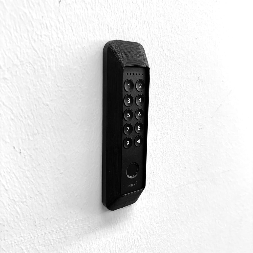 Nuki Keypad 2 im schwarzen Diebstahlschutz an weißer Wand montiert, Schrägansicht von links