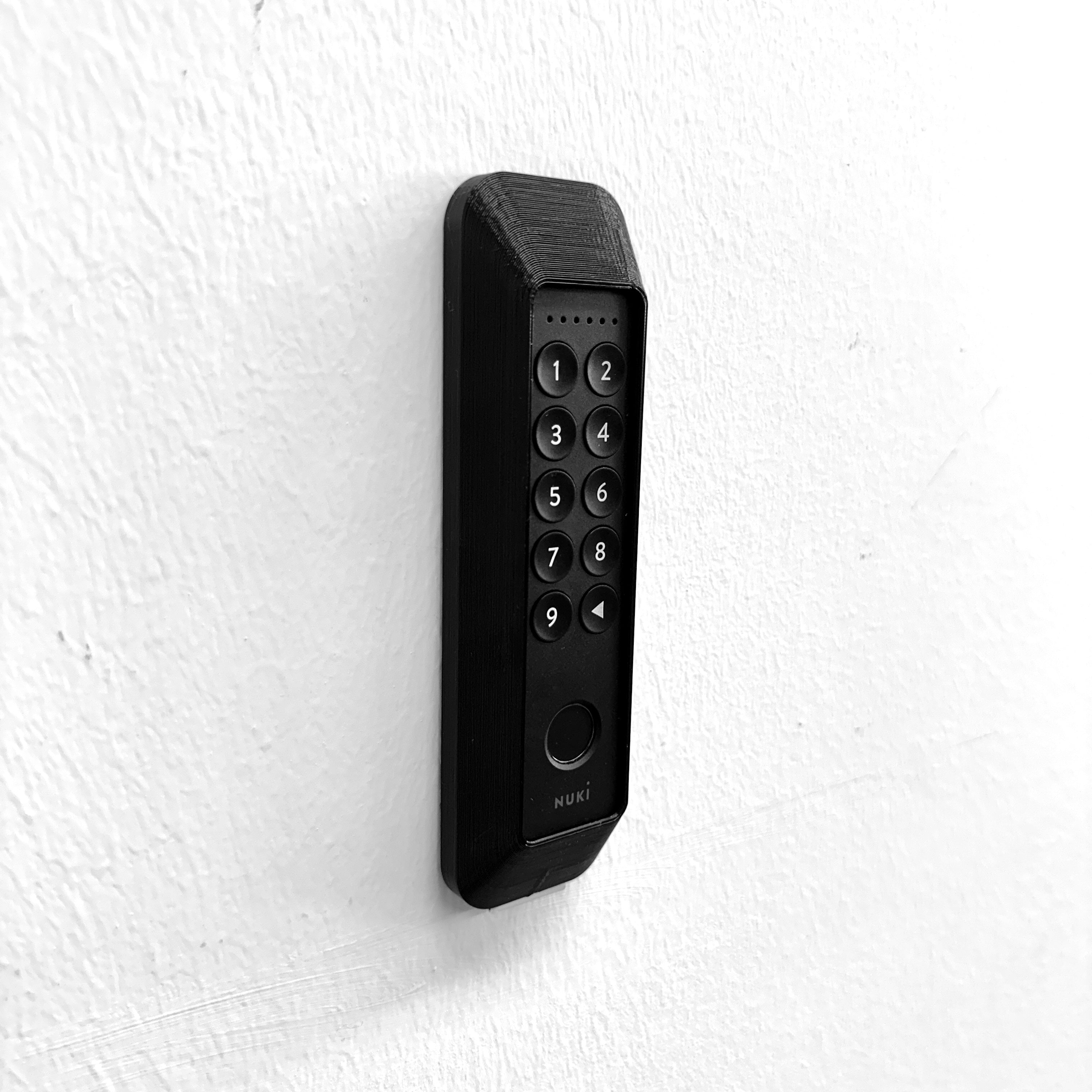Nuki Keypad 2 im schwarzen Diebstahlschutz an weißer Wand montiert, Schrägansicht von links