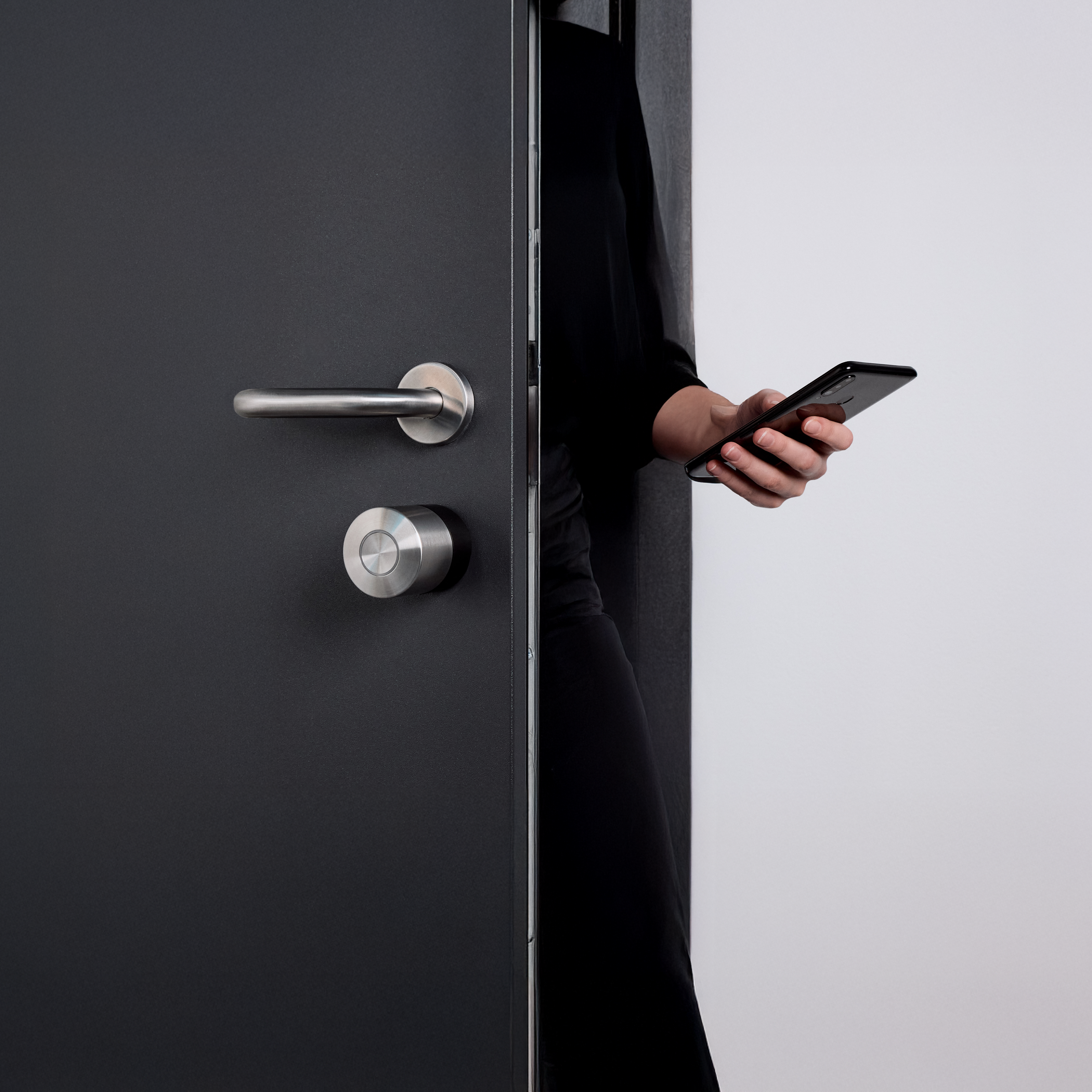 Dunkle Wohnungstür mit montiertem Nuki Smart Lock Pro, davor eine Person mit Smartphone in der Hand