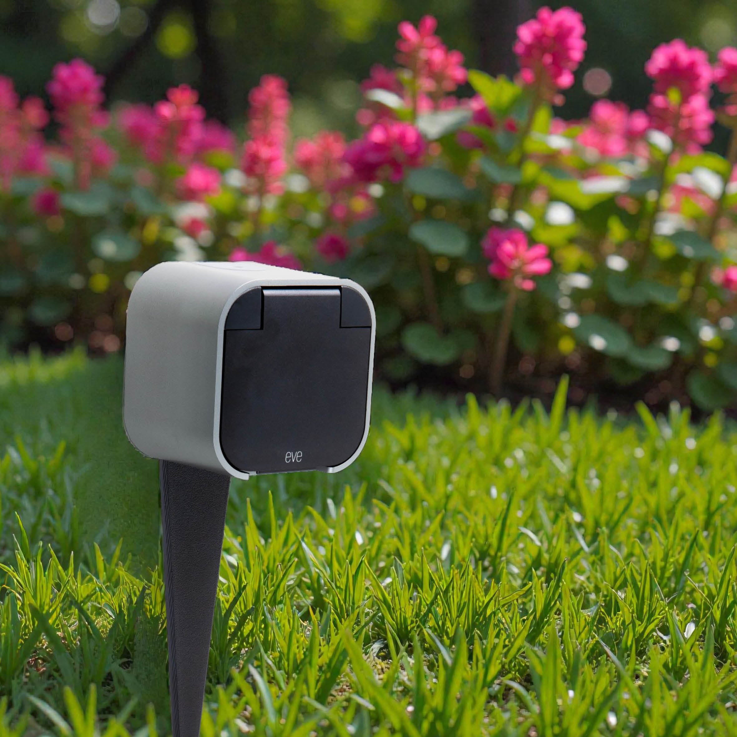 Eve Energy Outdoor auf dem Erdspieß im Beet vor blühenden Blumen